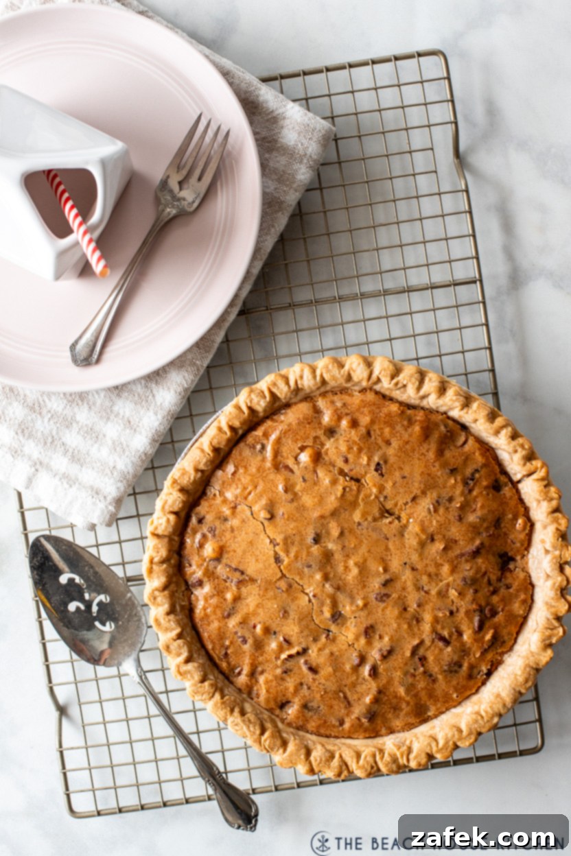 Ultimate Chocolate Chip Delight 8 Overhead photo of a freshly baked chocolate chip pie cooling on a wire rack, with a single slice on a plate next to a fork and a container of milk.