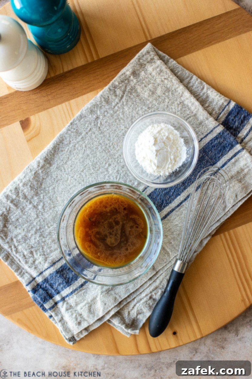 Overhead photo of a small bowl containing a cornstarch slurry with a whisk, alongside a bowl of rich beef gravy, illustrating the gravy thickening process