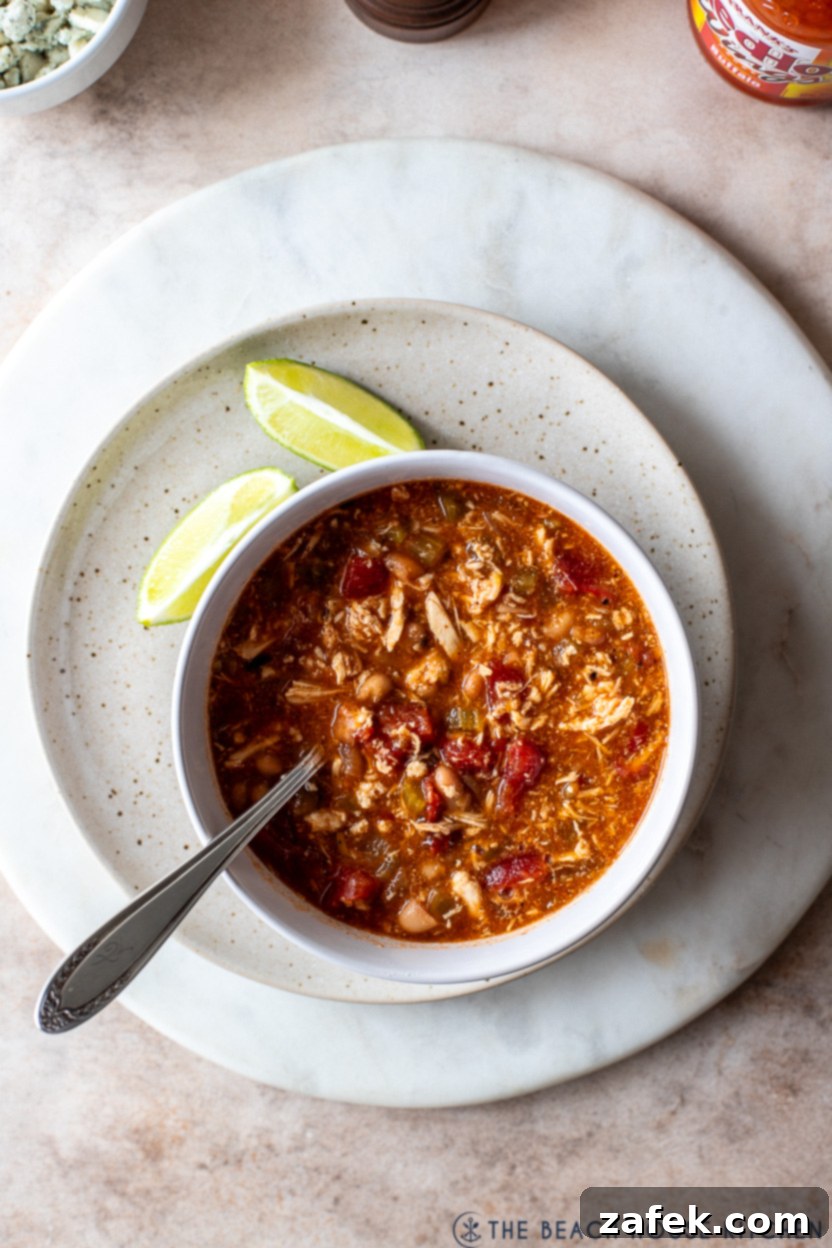 Overhead photo of a bowl of buffalo chicken chili on a plate with two lime slices, ready to be eaten
