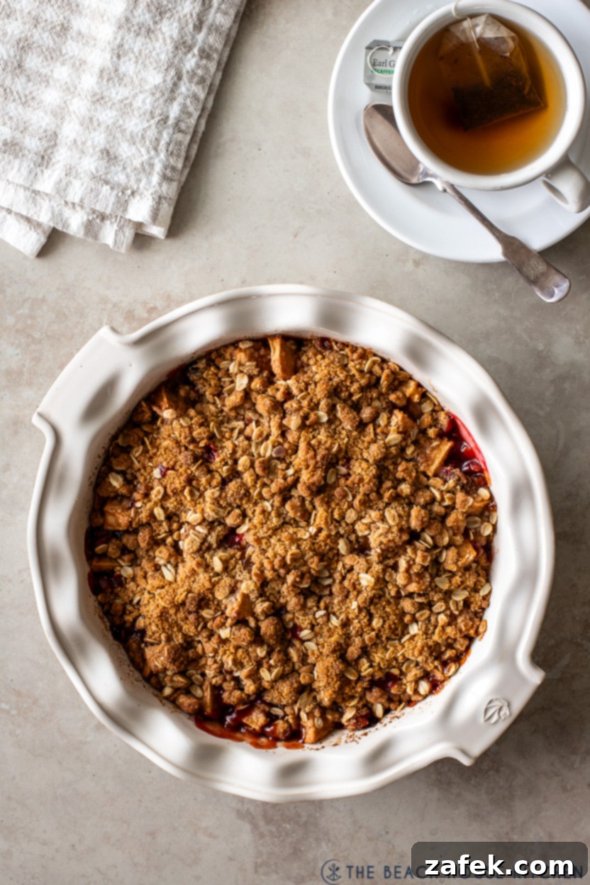 Spiced Apple Cranberry Crisp 11 Overhead photo of a freshly baked apple cranberry crisp next to a steaming cup of tea, set on a rustic wooden surface