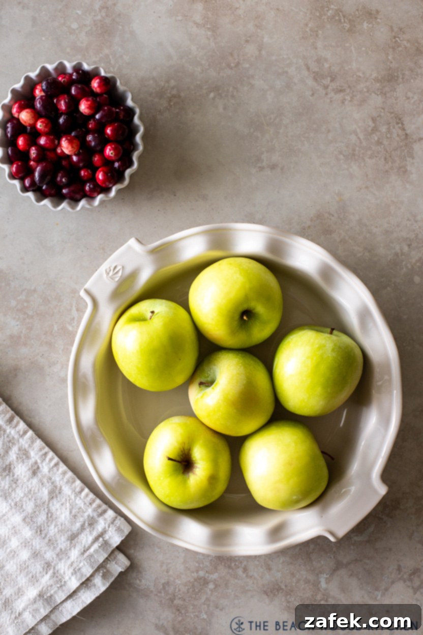 Spiced Apple Cranberry Crisp 3 Overhead photo of a bowl of fresh cranberries next to a pie plate filled with sliced Granny Smith apples