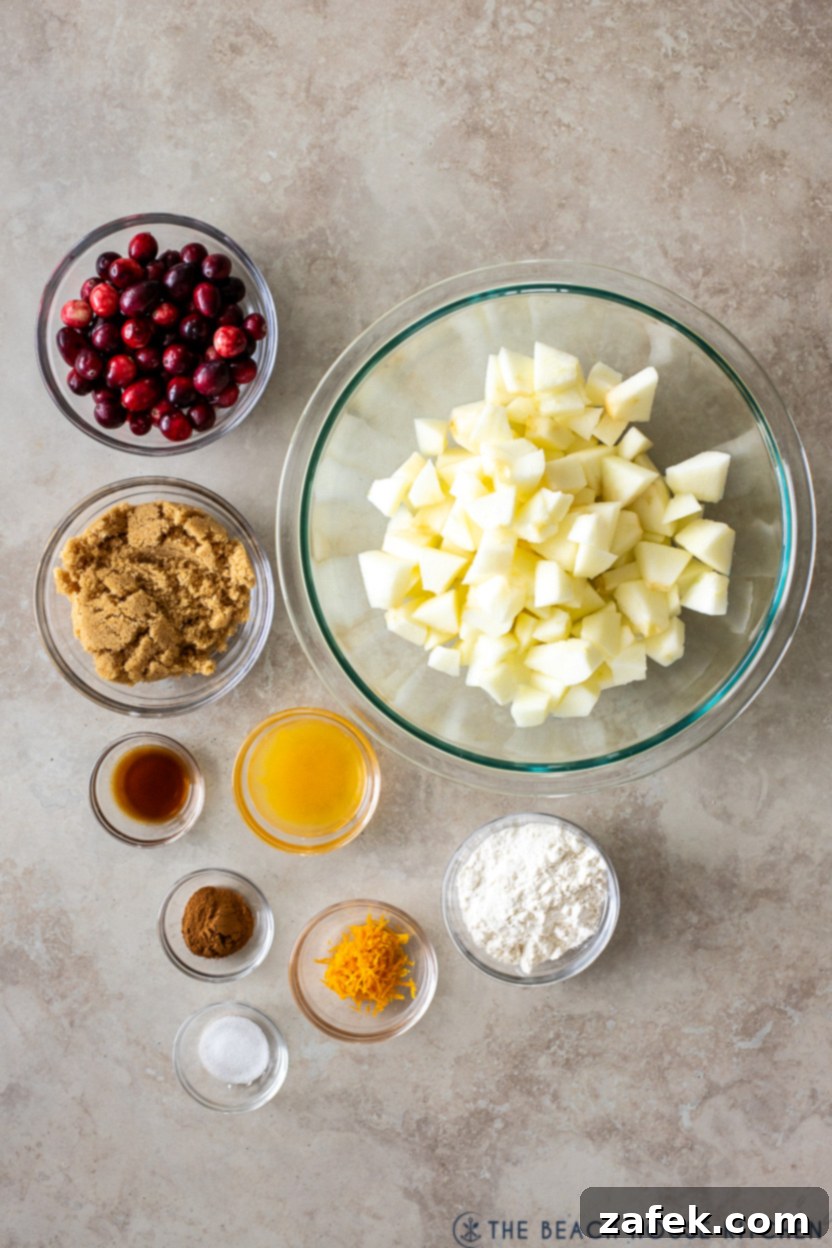 Spiced Apple Cranberry Crisp 5 Overhead photo of ingredients for apple cranberry crisp filling: sliced apples, fresh cranberries, brown sugar, flour, cinnamon, salt, vanilla extract, orange zest, and orange juice